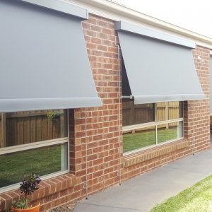 Awning blinds installed outdoors on the windows of a brick home